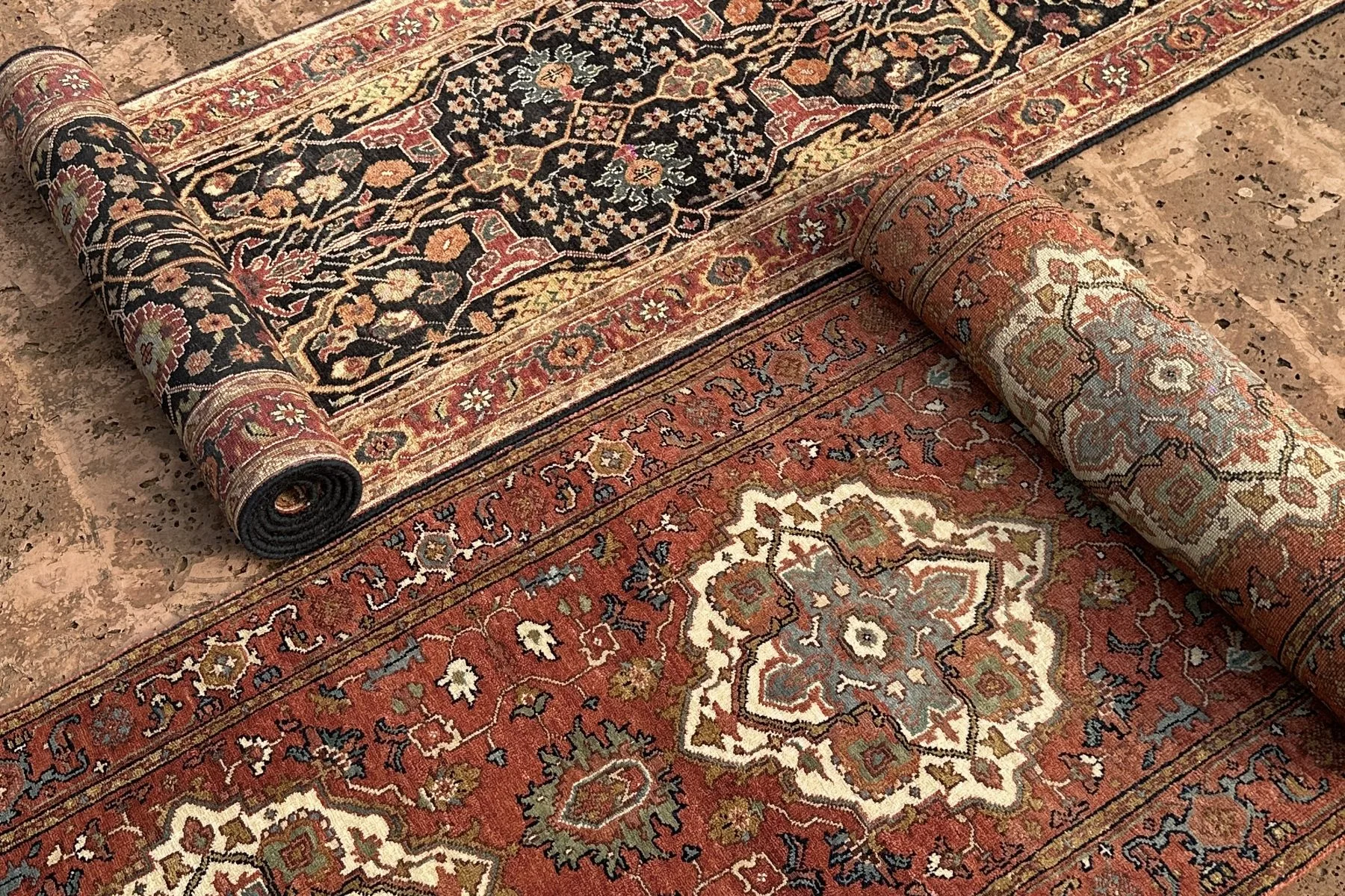 Hand-knotted rugs unrolled, with one rug rolled at the edge